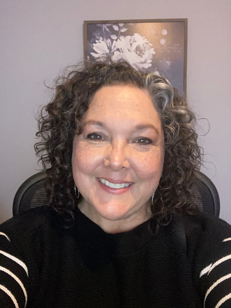 Headshot of a white female with curly brown hair and a dark sweater.
