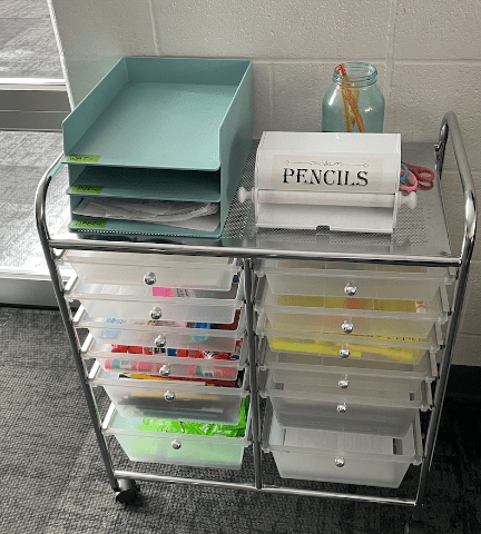 12 drawer shelf with a box labeled pencils on it and items in the drawers.